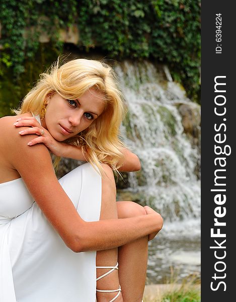 Woman in white dress sitting near waterfall