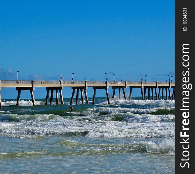 Surfer riding the waves near a pier on a bright sunny day. Surfer riding the waves near a pier on a bright sunny day