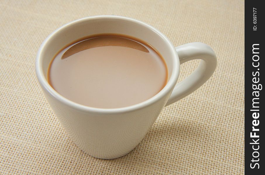 White cup of hot coffee milk on the table covered by cloth. White cup of hot coffee milk on the table covered by cloth
