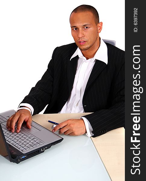 A young businessman sitting by desk at office working on the laptop with cellphone in his hand. Isolated over white. A young businessman sitting by desk at office working on the laptop with cellphone in his hand. Isolated over white.