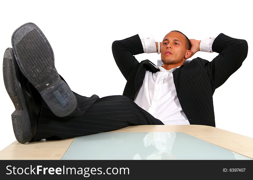 A young satisfied businessman sitting by desk at office feet on table thinking. Isolated over white. A young satisfied businessman sitting by desk at office feet on table thinking. Isolated over white.