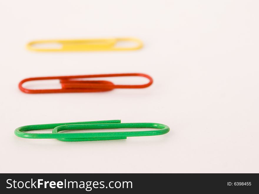 Green,red and yellow paper clips on white background shallow focal plane with front green one in focus. Green,red and yellow paper clips on white background shallow focal plane with front green one in focus