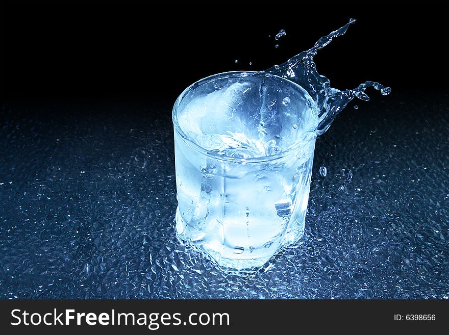 Glass of cold splashing water standing on dark background