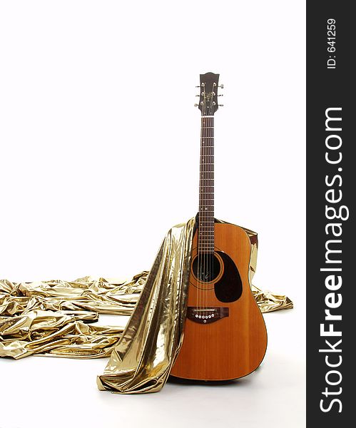 Acoustic guitar with gold material draped over. Acoustic guitar with gold material draped over
