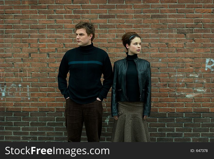 Pair in stylish autumn outfit posing in front of a brick wall. Pair in stylish autumn outfit posing in front of a brick wall