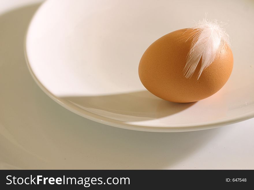 Egg with feather on a plate lighten by hard light. Egg with feather on a plate lighten by hard light