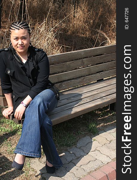 Beautiful Asian girl with braids sitting on park bench