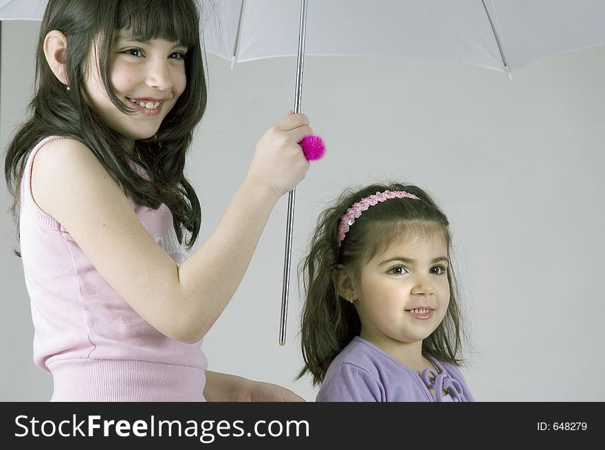 Two little sisters holding an umbrella and smiling happily. Two little sisters holding an umbrella and smiling happily.