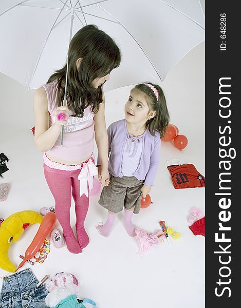 Two cute little sisters playing with a white umbrella, surrounded by colourful toys. Two cute little sisters playing with a white umbrella, surrounded by colourful toys.