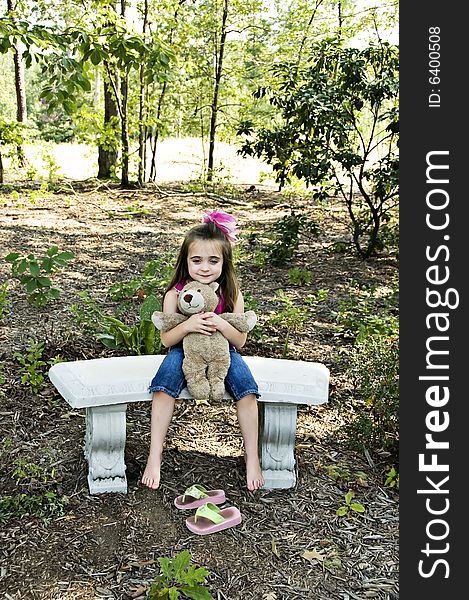 Cute little brunette girl holding her best friend a teddy bear sitting with bare feet in an outdoor setting. Cute little brunette girl holding her best friend a teddy bear sitting with bare feet in an outdoor setting.