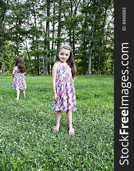 Two little girls standing in a garden with identical dresses.  One facing front and the other facing back. Two little girls standing in a garden with identical dresses.  One facing front and the other facing back.