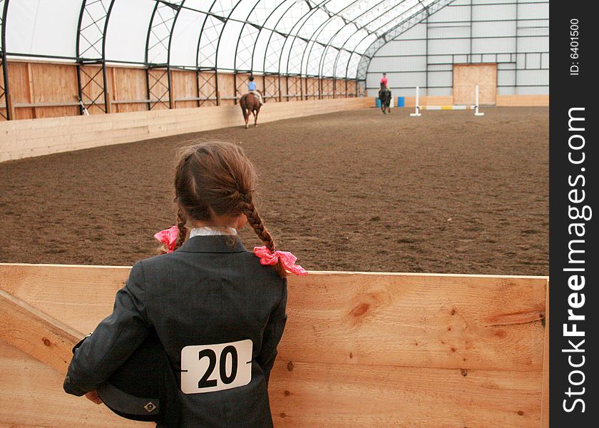 A young woman in pigtails with pink ribbons, holding her riding helmet and waiting to be called to the show ring. A young woman in pigtails with pink ribbons, holding her riding helmet and waiting to be called to the show ring