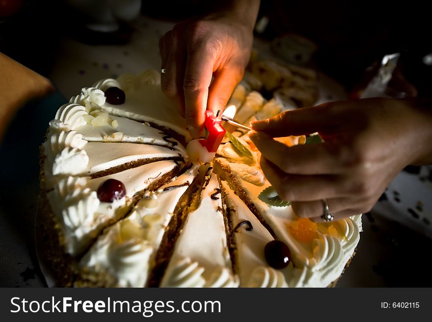 Closeup of birthday cake with hands lighting candle