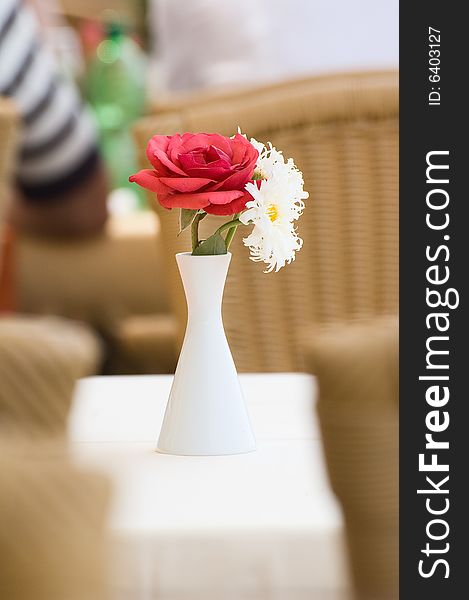 Photo of a bouquet of one rose and two camomiles in the vase standing at the dinner table. Photo of a bouquet of one rose and two camomiles in the vase standing at the dinner table