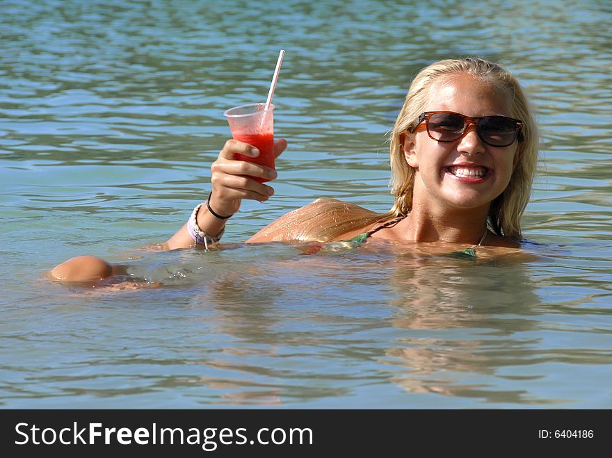 A blond girl is drinking strawberry cocktail in the water