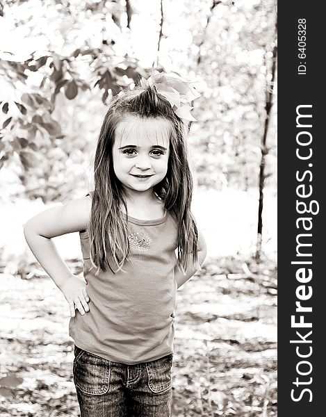 Beautiful little brunette girl with a pink bow and shirt standing outdoors with her hands on her hips. Beautiful little brunette girl with a pink bow and shirt standing outdoors with her hands on her hips.