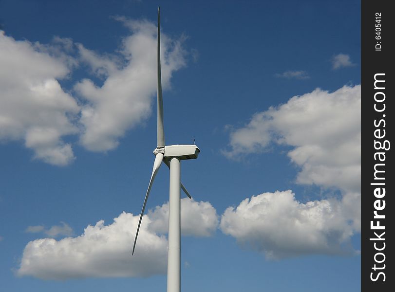 A photo  of a Wind Turbine with a blue sky and clouds in the background.