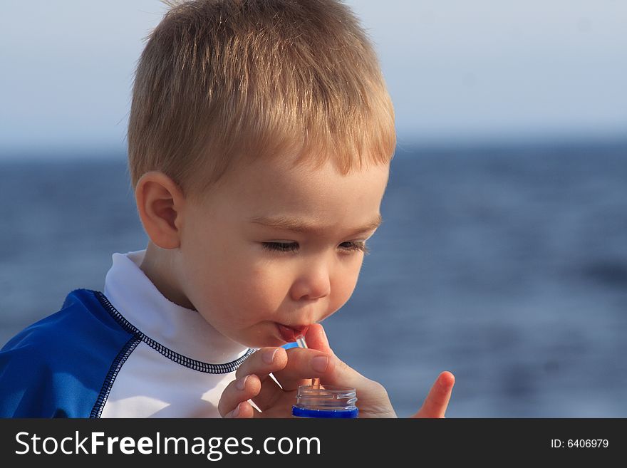 A toddler boy drinking juice through a straw while at the beach. A toddler boy drinking juice through a straw while at the beach.