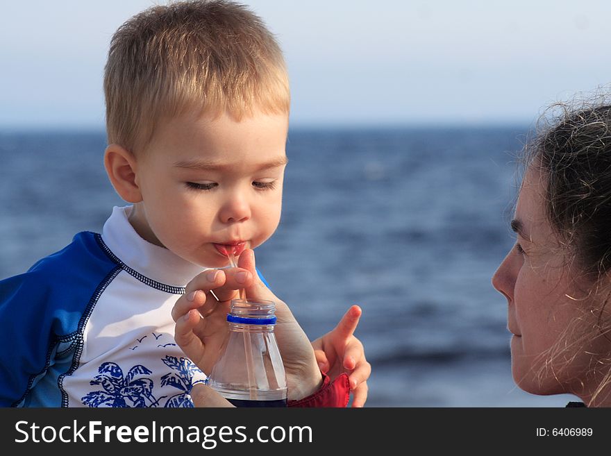 A toddler boy drinking juice through a straw while at the beach. A toddler boy drinking juice through a straw while at the beach.