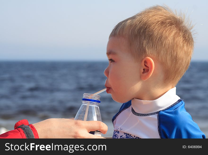 A toddler boy drinking juice through a straw while at the beach. A toddler boy drinking juice through a straw while at the beach.