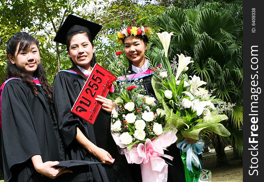 Gorgeous Asian university graduates celebrating their success. Number plate says Happy Graduation in Thai and the number refers to this year.