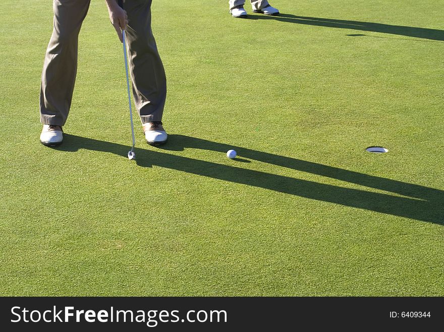 A man is standing on the green of a golf course.  He is putting the ball into the hole.  Horizontally framed shot. A man is standing on the green of a golf course.  He is putting the ball into the hole.  Horizontally framed shot.