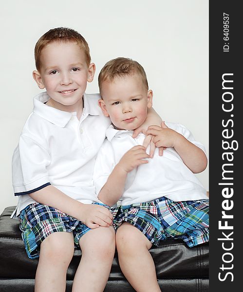 Two young brothers are posing together for a picture in a studio. They are wearing matching outfits and smiling at the camera. Vertically framed shot. Two young brothers are posing together for a picture in a studio. They are wearing matching outfits and smiling at the camera. Vertically framed shot.