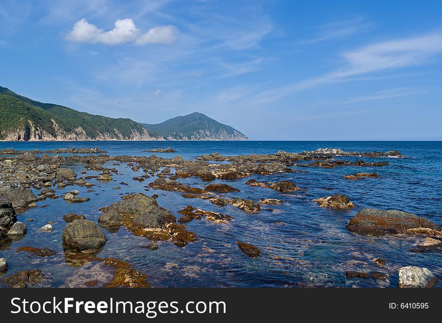 Seacoast of Japanese sea. On foreground are very many stones among seawater. On backgrouns are rocky bank and green cape. Seacoast of Japanese sea. On foreground are very many stones among seawater. On backgrouns are rocky bank and green cape.