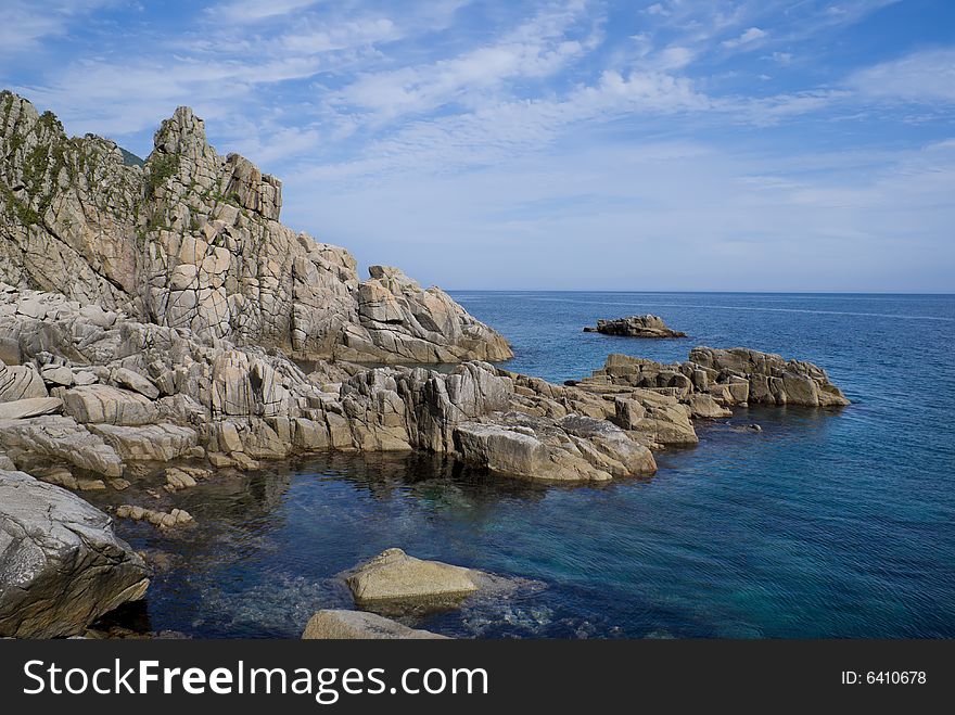 A landscape on Japanese sea. On foreground is long rocky cape. On background are seawater an blue sky with clouds. A landscape on Japanese sea. On foreground is long rocky cape. On background are seawater an blue sky with clouds.