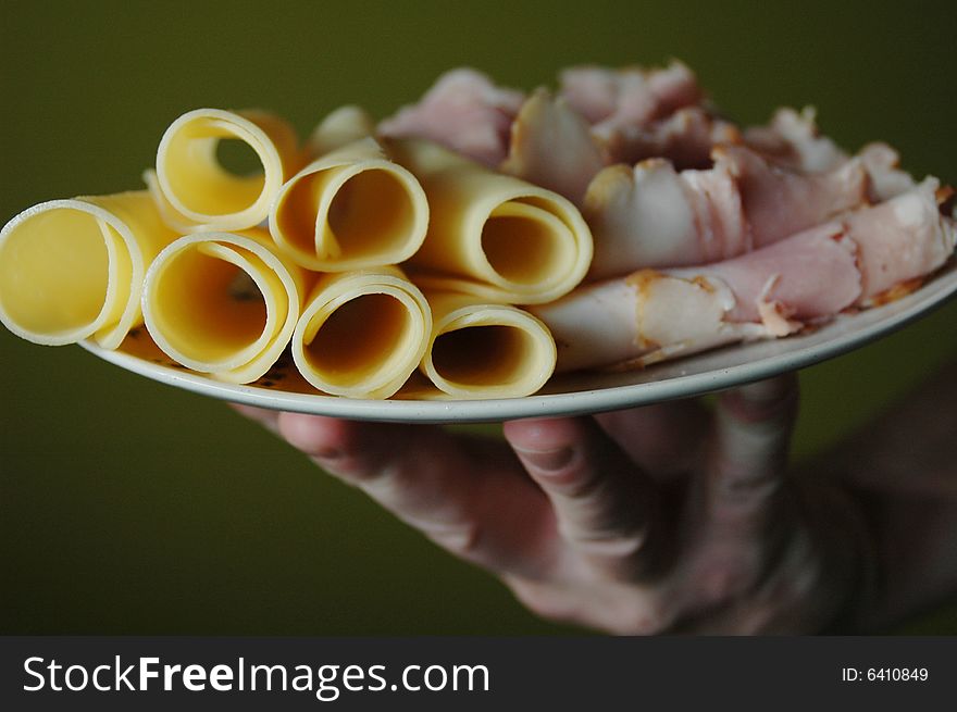 Slices of yellow cheese and ham on a plate held by a man's hand. Slices of yellow cheese and ham on a plate held by a man's hand