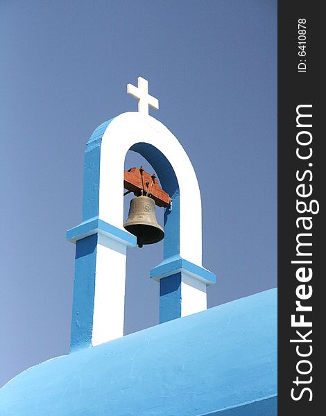 Greek church roof with cross and bell against the blue sky