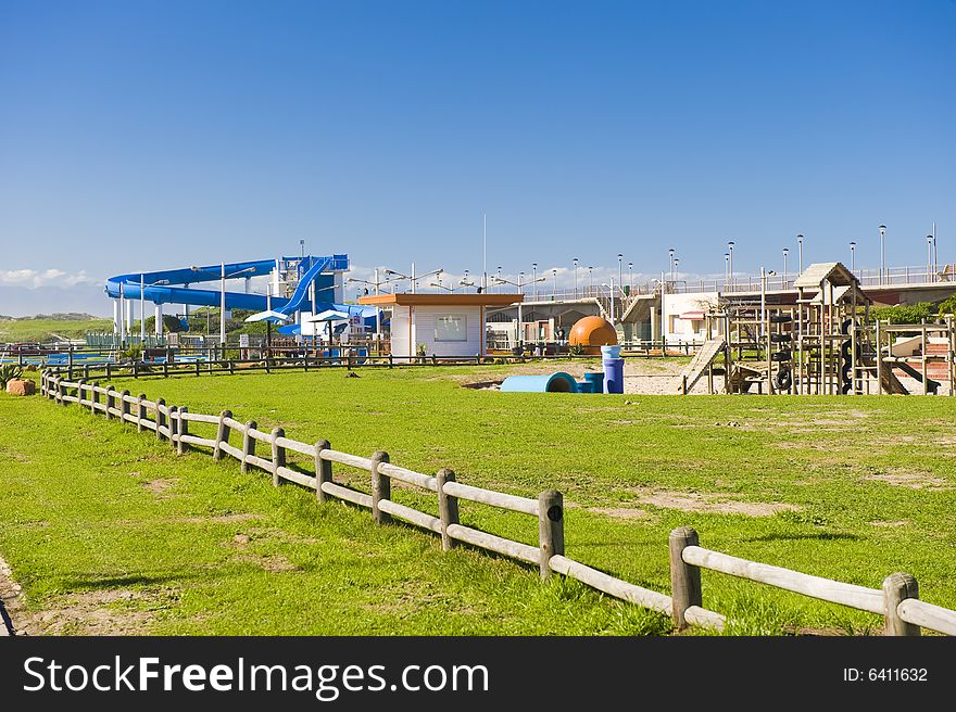 A park next to the beach with a play area for kids containing a wooden jungle-jim and a water slide. A park next to the beach with a play area for kids containing a wooden jungle-jim and a water slide.