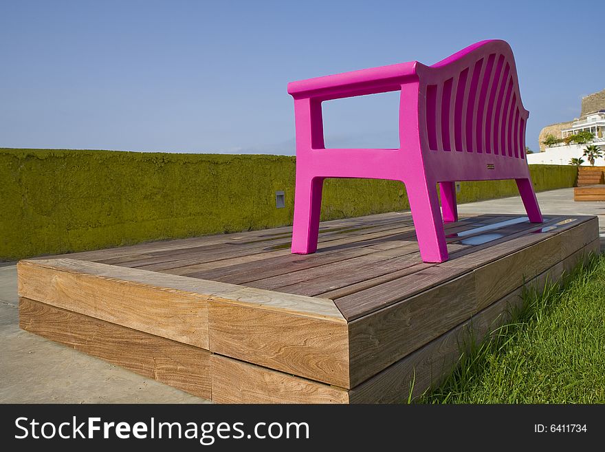 Solitarie plastic pink bench on a park with wood stand