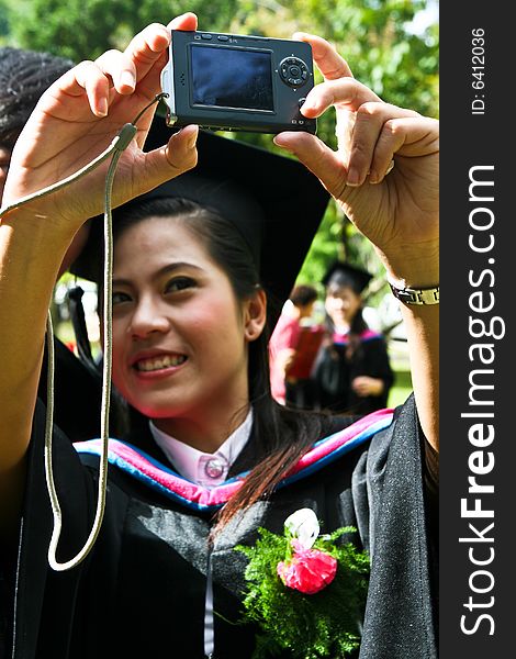 Beautiful young Asian graduate takes a photo of herself on graduation day (focus on camera).