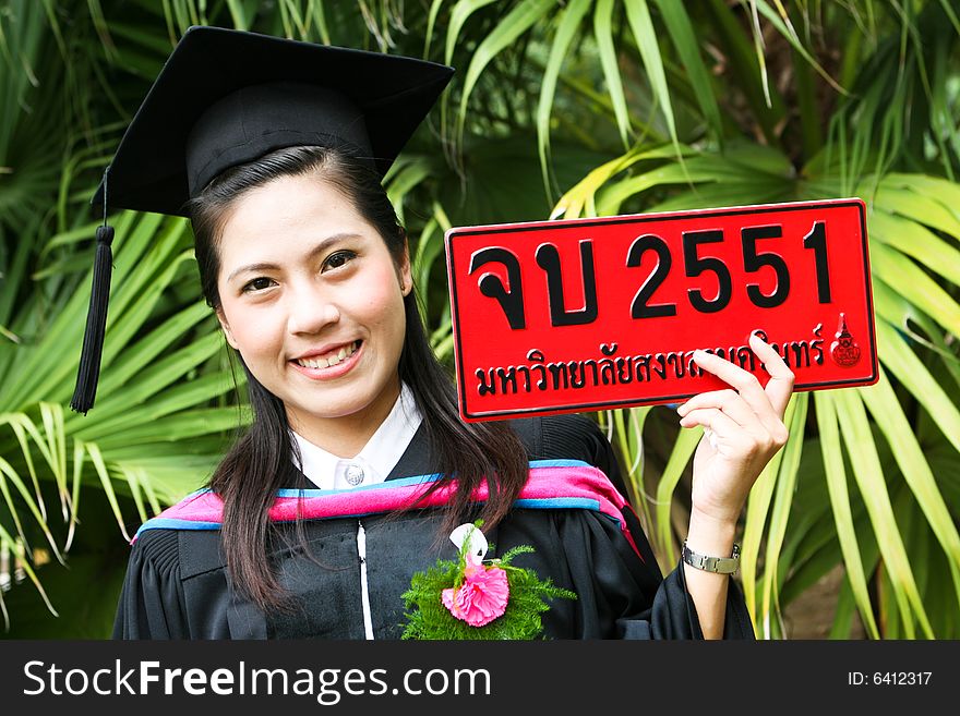 Beautiful young Asian graduate in robes on graduation day. Number plate says Happy Graduation in Thai and number refers to the year.