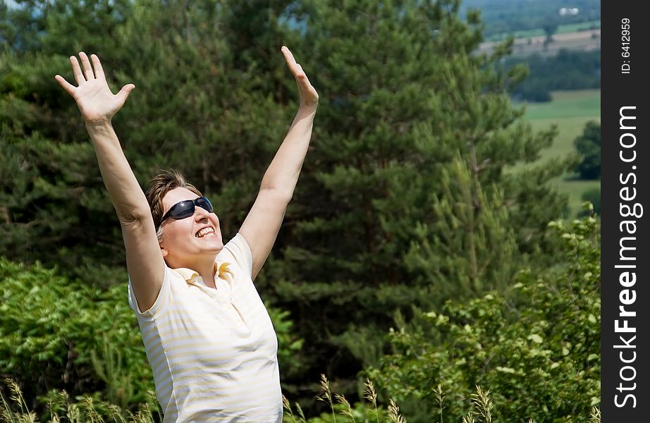 Woman with arms outstretched standing on the hill. Green forest on background. Summer. Woman with arms outstretched standing on the hill. Green forest on background. Summer.