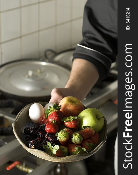 Chef's arm holding out a fruit plate with apples, strawberries, eggs, and blackberries on it. Vertically framed photo. Chef's arm holding out a fruit plate with apples, strawberries, eggs, and blackberries on it. Vertically framed photo.