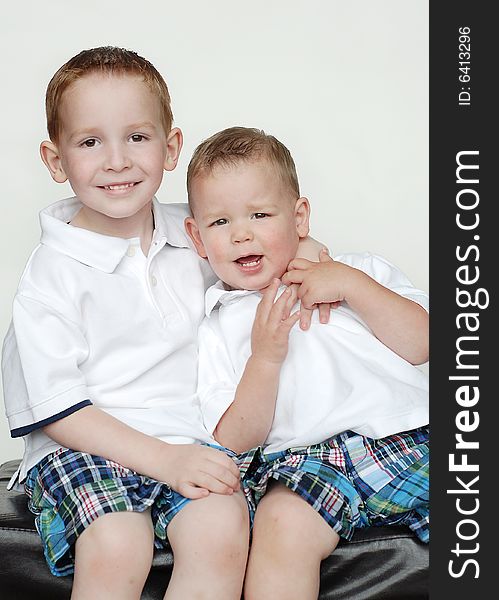 Two young brothers are posing together for a picture in a studio. They are wearing matching outfits and smiling at the camera.  Vertically framed shot. Two young brothers are posing together for a picture in a studio. They are wearing matching outfits and smiling at the camera.  Vertically framed shot.