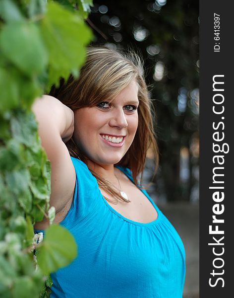 Young woman leaning against a vine covered wall with a sultry smile on her face. Vertically framed photo. Young woman leaning against a vine covered wall with a sultry smile on her face. Vertically framed photo.