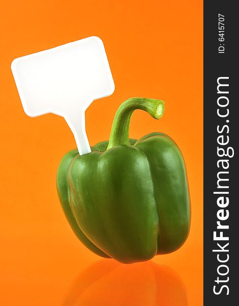 Green paprika against orange background with price tag
