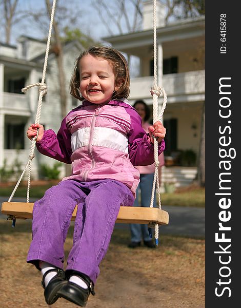 Cute little girl swinging on rope swing, mom out of focus in background