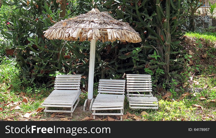 Thatched umbrella and three wooden chairs in a park. Thatched umbrella and three wooden chairs in a park.