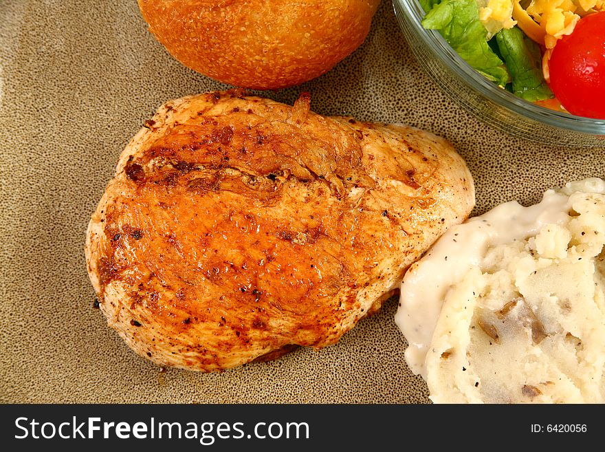 Grilled chicken, mashed potatoes, rolls and salad in plate.