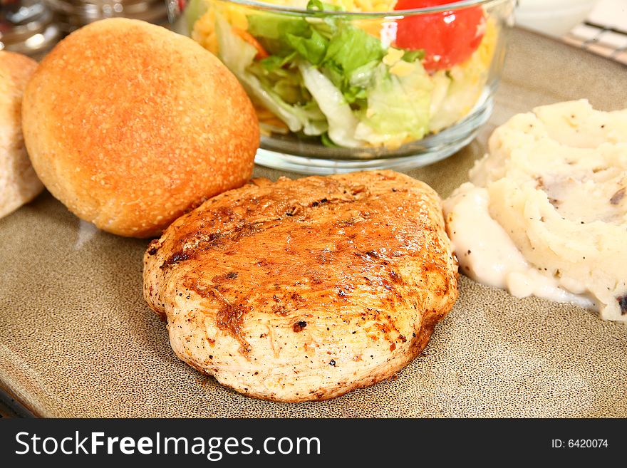 Grilled chicken, mashed potatoes, rolls and salad in plate.