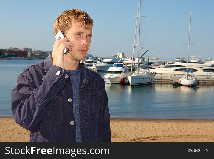 Young stylish man talk on mobile phone with yacht background.