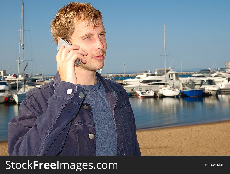 Young stylish man talk on mobile phone with yacht background.