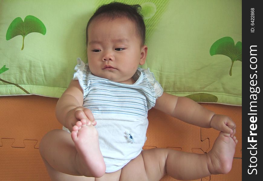 Lovely baby is lying down on a pillow playing her feet