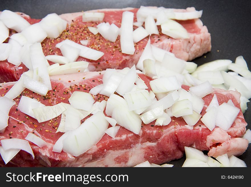 Fresh strip steaks smothered in onions in a pan. Fresh strip steaks smothered in onions in a pan