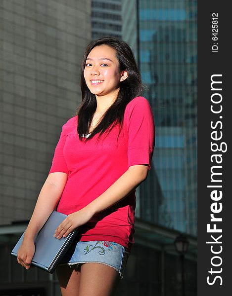 Picture of an Asian Girl carrying a notebook with office landscape behind. Suitable for contexts of office environment, casual staff, part-timers, and even interns. Picture of an Asian Girl carrying a notebook with office landscape behind. Suitable for contexts of office environment, casual staff, part-timers, and even interns.