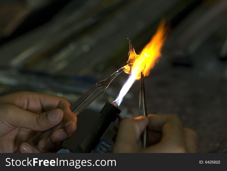 Artist shaping hot glass into a figurine, using a gass flame. Artist shaping hot glass into a figurine, using a gass flame.